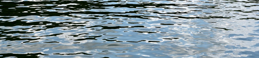 Photograph of the lake surface showing ripples and reflections of sky and clouds.